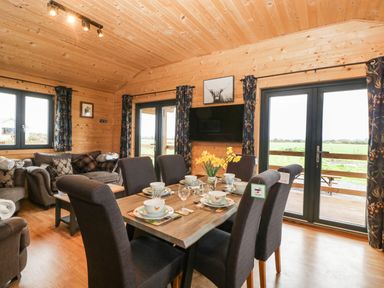 A dining table set for six with flowers in a wooden room next to a sitting area with sofas and windows at The Lodge at Crossroads Farm in Middlezoy