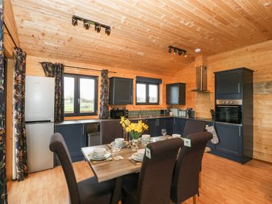 A kitchen and dining area with wooden walls and ceiling dark cabinets dining table set with dishes and flowers at The Lodge at Crossroads Farm in Middlezoy