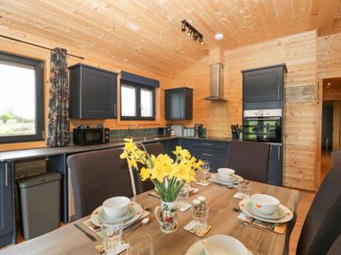 A kitchen and dining area with wooden walls and ceiling and a table set for four with yellow flowers at The Lodge at Crossroads Farm in Middlezoy