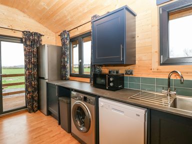 A kitchen with a refrigerator washing machine dishwasher microwave and sink with windows and curtains at The Lodge at Crossroads Farm in Middlezoy