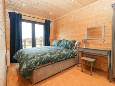 A bedroom with a bed green floral bedding navy curtains and a gray dressing table with a stool at The Lodge at Crossroads Farm in Middlezoy