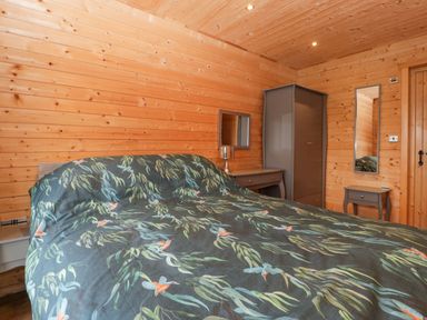 A bedroom with wood panel walls a bed with bird patterned bedding a gray wardrobe and a dressing table at The Lodge at Crossroads Farm in Middlezoy