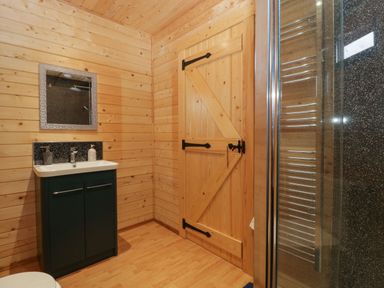 A bathroom with wooden walls and door a sink with cabinet a mirror and a shower at The Lodge at Crossroads Farm in Middlezoy