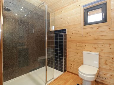 A bathroom with a shower enclosure and a toilet with wooden walls and a small window at The Lodge at Crossroads Farm in Middlezoy