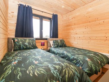 A bedroom with two single beds with botanical bedding and a window with curtains at The Lodge at Crossroads Farm in Middlezoy