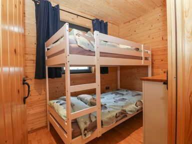 A small bedroom with a white bunk bed with animal printed bedding wooden walls and dark curtains at The Lodge at Crossroads Farm in Middlezoy