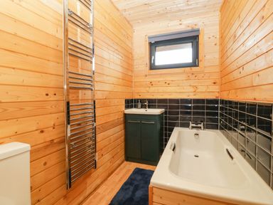 A bathroom with wooden walls a bathtub a sink with cabinet a heated towel rail and a small window at The Lodge at Crossroads Farm in Middlezoy