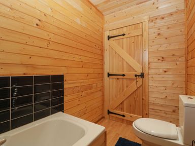 A bathroom with wooden walls a wooden door a white bathtub and a white toilet at The Lodge at Crossroads Farm in Middlezoy