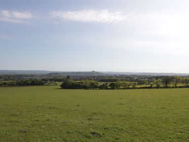 A large green field with trees in the distance and a town beyond under a blue sky at The Lodge at Crossroads Farm Middlezoy