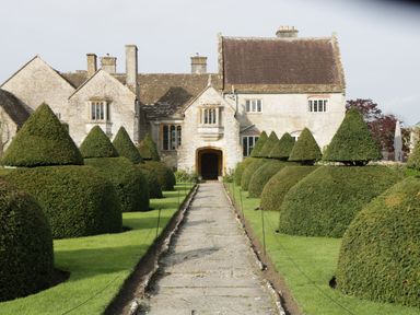 A stone pathway leading to a historic stone house with symmetrical cone and dome shaped shrubs on both sides at The Lodge at Crossroads Farm in Middlezoy