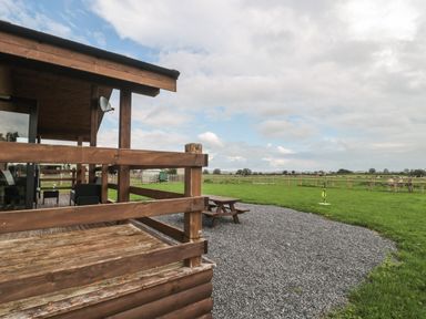 A wooden porch attached to a house with a gravel area and picnic table next to a fenced green field at The Lodge at Crossroads Farm in Middlezoy