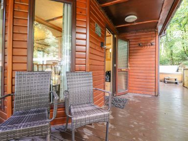 A porch area with two wicker chairs and a wooden hot tub on a deck outside a wooden cabin at Woodland Retreat in Skiptory Howe 41A White Cross Bay near Windermere