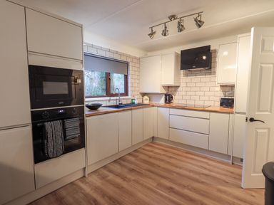 A kitchen with wooden flooring white cabinets a window above the sink and built in appliances at Woodland Retreat Skiptory Howe 41A White Cross Bay near Windermere
