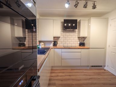 A kitchen with wood countertops white cabinets a black oven black toaster and kettle with tiled backsplash at Woodland Retreat Skiptory Howe 41A White Cross Bay near Windermere