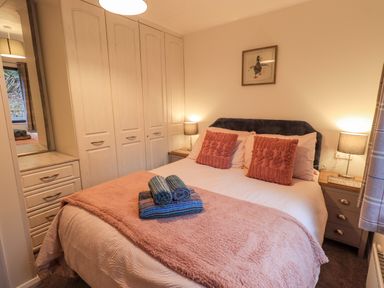 A bedroom with a double bed with pillows and folded towels on it bedside tables with lamps and built in wardrobes at Woodland Retreat Skiptory Howe 41A White Cross Bay near Windermere