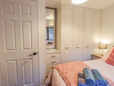 A bedroom with a closed door white wardrobes a bed with pink bedding and rolled towels at Woodland Retreat Skiptory Howe 41A White Cross Bay near Windermere