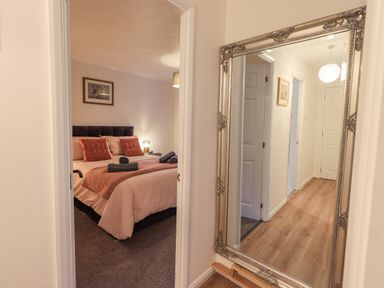 A hallway with a large ornate mirror reflecting doors and a hallway leading to a bedroom with a bed and cushions at Woodland Retreat Skiptory Howe 41A White Cross Bay near Windermere