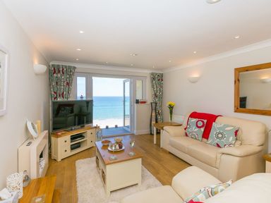 A living room with cream sofas and a coffee table overlooking the sea at Surf and Sand in Carbis Bay