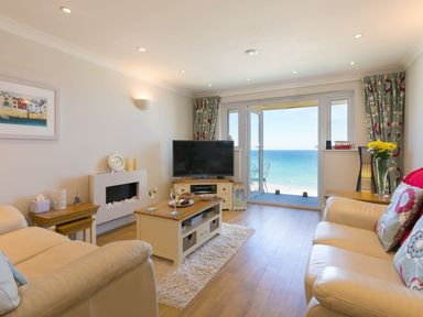 A living room with cream sofas coffee table and television with sea view at Surf and Sand in Carbis Bay