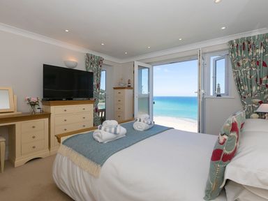 A bedroom with a bed facing open doors to a sea view at Surf and Sand in Carbis Bay