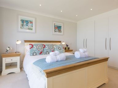 A bedroom with a double bed with blue floral pillows and white rolled towels on a blue blanket at Surf and Sand in Carbis Bay