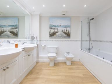 A bathroom with two sinks a toilet a bidet a bathtub with a shower and a beach painting on the wall at Surf and Sand in Carbis Bay