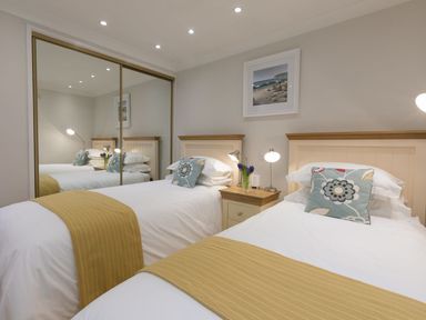A bedroom with two single beds a nightstand with lamps and flowers and mirrored wardrobe at Surf and Sand in Carbis Bay