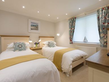 A bedroom with two single beds nightstand lamps window with curtains and a dresser at Surf and Sand in Carbis Bay