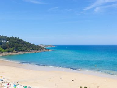 A beach with people on the sand and near the water by a rocky coastline and blue sea at Surf and Sand in Carbis Bay
