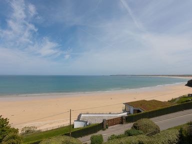 A sandy beach with a calm sea and a building with a green roof near a road at Surf and Sand in Carbis Bay