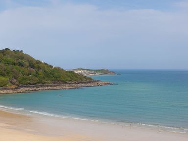 A beach with sand and calm sea water with green hills on the left at Surf and Sand in Carbis Bay