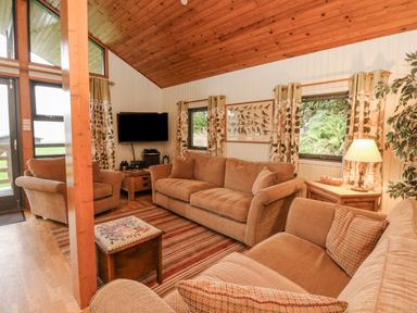 A living room with sofas a TV wooden ceiling and windows with curtains at Firbush Lodge in Killin