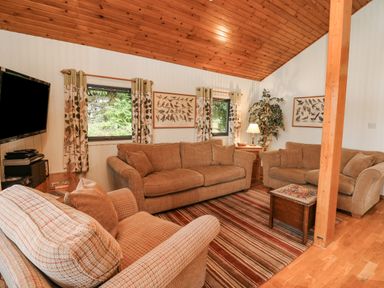 A living room with three sofas a striped rug and a wooden ceiling at Firbush Lodge in Killin