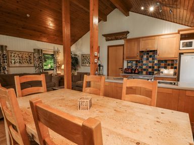 A wooden dining table with chairs in an open plan kitchen and living area with tiled kitchen backsplash at Firbush Lodge in Killin