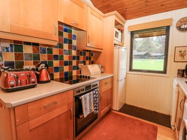 A kitchen with wooden cabinets a colorful tiled backsplash appliances and a window with a view at Firbush Lodge in Killin