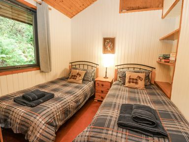 A bedroom with two single beds bedside table with lamp and window showing greenery at Firbush Lodge in Killin