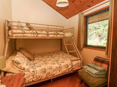 A bedroom with a bunk bed with floral bedding a green armchair with folded towels a window and wood paneled walls at Firbush Lodge in Killin