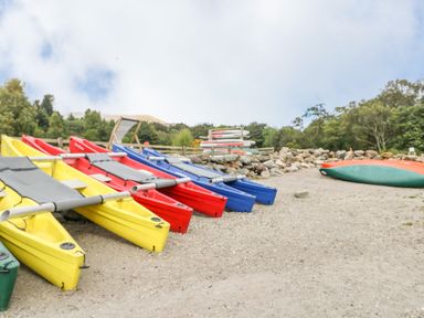Several colorful kayaks and paddleboards on a sandy and rocky area with trees in the background at Firbush Lodge in Killin