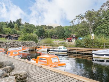 A small harbour with boats docked and a tractor near trees and wooden cabins at Firbush Lodge in Killin