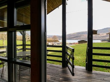 A wooden porch with a railing and table with chairs overlooking a grassy area and lake at Firbush Lodge in Killin