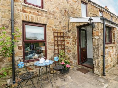 A stone cottage exterior with a small patio table and two chairs near a door at Dunnock Cottage in Broad Haven