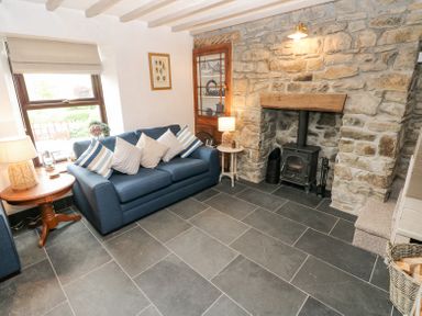 A living room with a blue sofa and striped pillows next to a fireplace with stone walls at Dunnock Cottage in Broad Haven