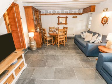 A living room with a wooden dining table and chairs a blue sofa a wooden cabinet and a television at Dunnock Cottage in Broad Haven