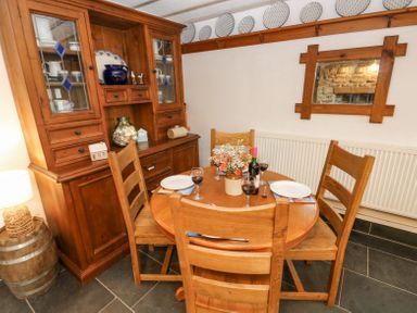 A dining room with a wooden table and chairs a wooden cabinet and a mirror on the wall at Dunnock Cottage in Broad Haven