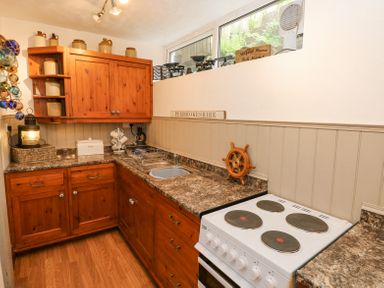 A kitchen with wooden cabinets a white stove a sink and various kitchen items at Dunnock Cottage in Broad Haven
