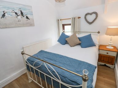 A bedroom with a white metal bed frame a blue quilt and cushions a wooden bedside table with a lamp and wall decorations at Dunnock Cottage Broad Haven