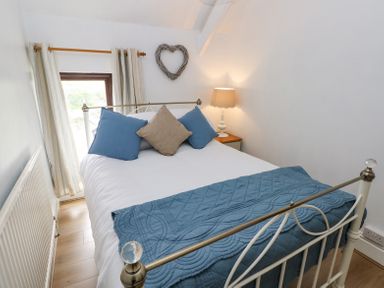 A bedroom with a white metal bed frame blue and beige pillows a blue quilted throw and a bedside lamp at Dunnock Cottage in Broad Haven