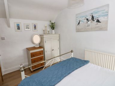 A bedroom with a bed, a white and wood chest of drawers, a white cupboard, framed pictures on the wall and a painting of seabirds at Dunnock Cottage in Broad Haven