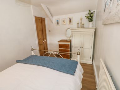 A bedroom with a bed a wooden wardrobe a chest of drawers and framed pictures on the wall at Dunnock Cottage in Broad Haven