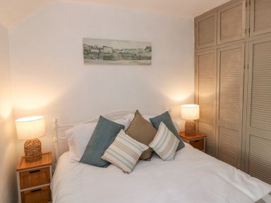 A bedroom with a double bed with pillows two bedside tables with lamps and built in wardrobes at Dunnock Cottage in Broad Haven